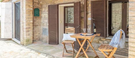 A stone building with wooden shutters, a table with chairs, and a bottle of wine.