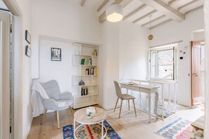 A room with a white chair, a small round table, a bookshelf, and a desk with a chair. - La Terrazza nel Borgo (Marsciano)