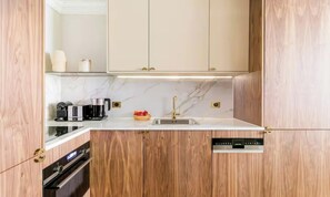 A kitchen with wooden cabinets, a marble countertop, a sink, a coffee maker, and a dishwasher. - A REFINED CONTEMPORARY DESIGN WITH THE TIMELESS CHARM OF PARIS - MARAIS (Paris)