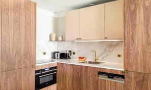 A modern kitchen with wooden cabinets, a marble countertop, a built-in oven, a coffee maker, a toaster, and a dishwasher. - A REFINED CONTEMPORARY DESIGN WITH THE TIMELESS CHARM OF PARIS - MARAIS (Paris)