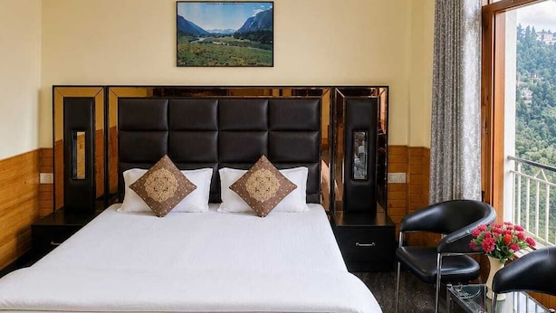 Een hotelkamer met een groot bed, een plafondventilator, een schilderij aan de muur, een raam met uitzicht en een paar slippers op de vloer.