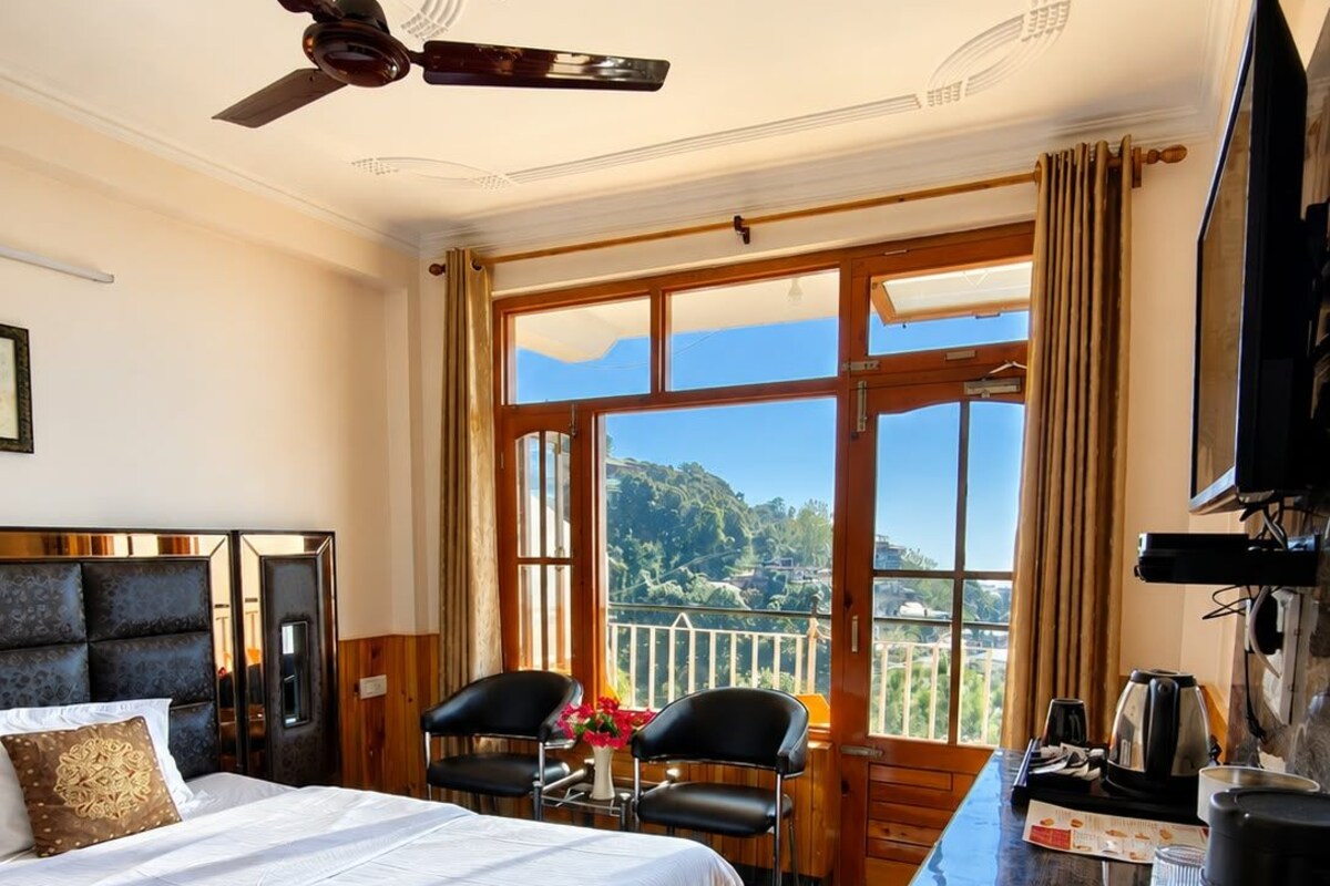 A hotel room with a bed, a desk, a television, and a view of a mountainous landscape.
