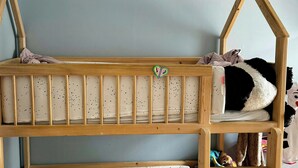 Een stapelbed met een hoofdbord in de vorm van een huis, een kleine rode kruk en verschillende knuffeldiertjes.