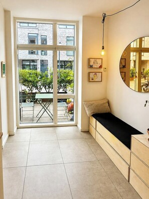 Une pièce dotée d’une porte-fenêtre coulissante donnant sur un espace extérieur, d’un canapé avec un coussin, d’un miroir rond accroché au mur et d’un luminaire.