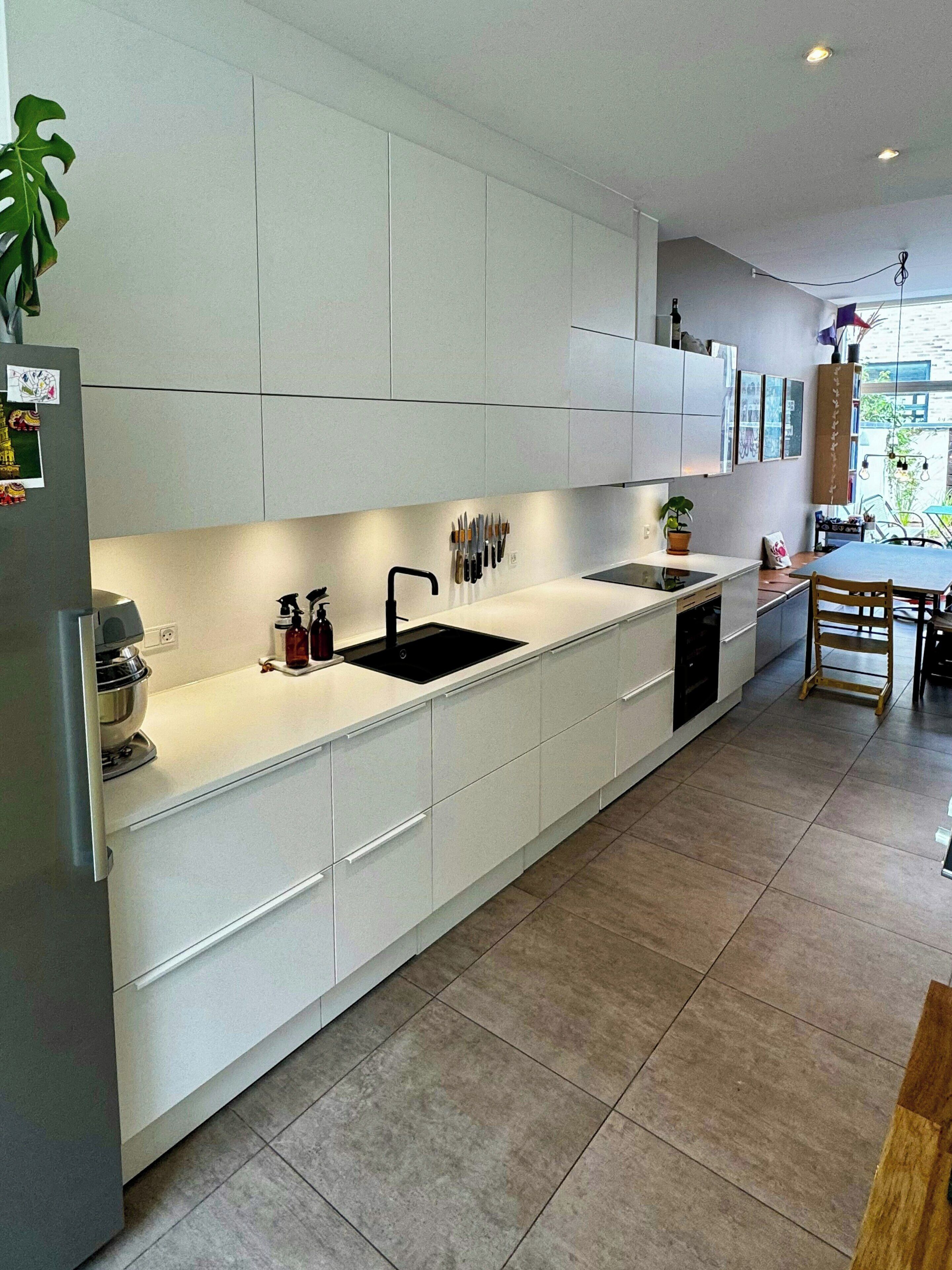A modern kitchen with white cabinetry, a black sink, and a dining area with a wooden table and chairs.