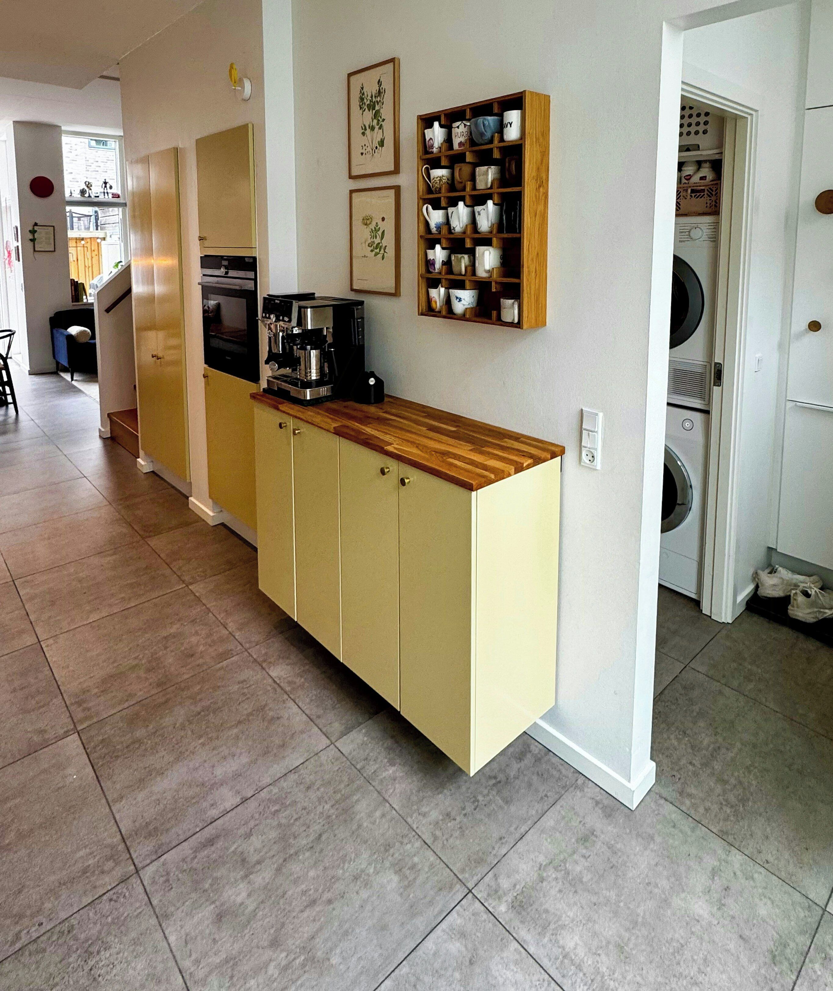 A kitchen with a built-in coffee machine, a wooden countertop, and a wall-mounted mug rack.