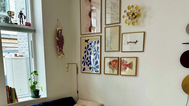Een moderne woonkamer met een modulaire bank, een potplant en diverse kunstwerken in lijsten aan de muur.