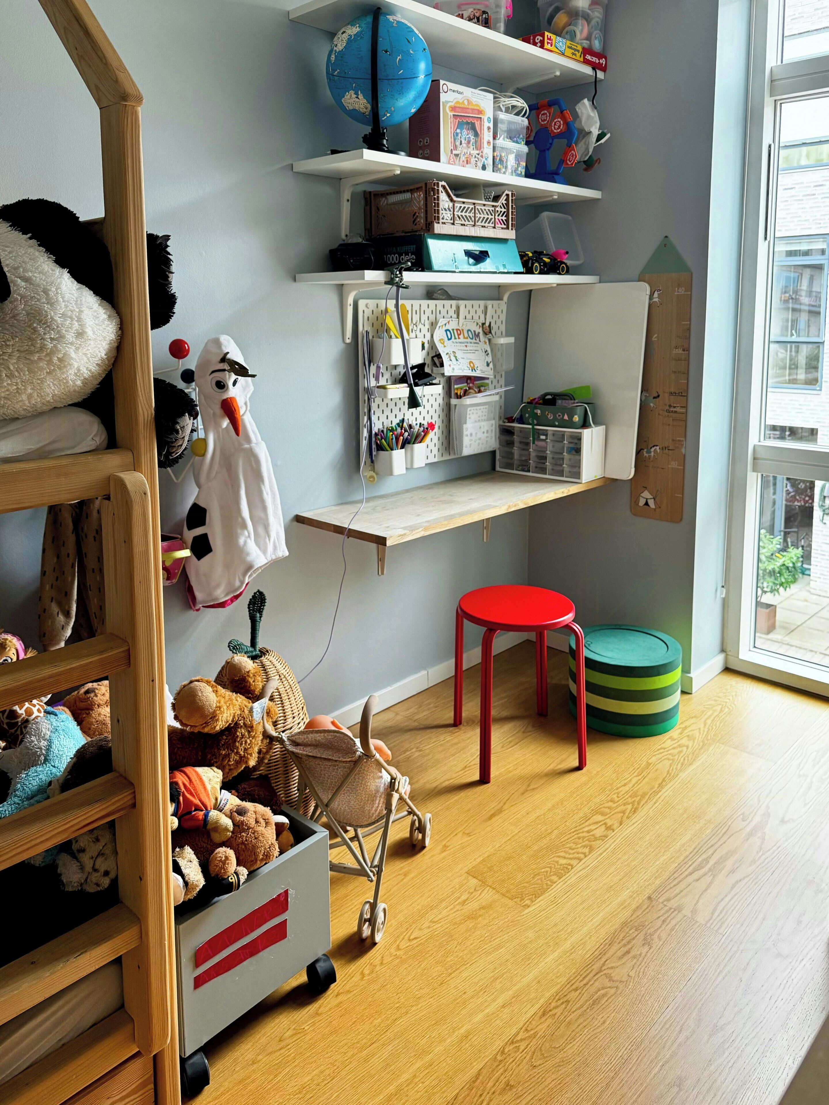 A child's room with a bunk bed, shelves with toys, a desk, and a window.
