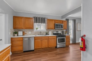 A kitchen with wooden cabinets, stainless steel appliances, and a dishwasher. - Clubhouse - All Star Baseball Rentals (Oneonta)