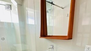 Un baño moderno con cabina de ducha de vidrio, lavamanos blanco sobre encimera negra y espejo con marco de madera.