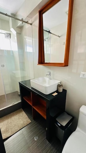 A modern bathroom with a glass shower enclosure, a white sink with a black countertop, and a wooden-framed mirror. - Ayra Hotel Boutique (Písac)
