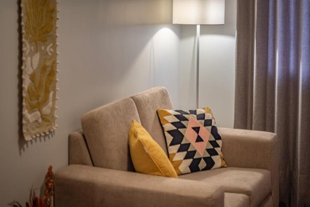 Un canapé beige avec deux coussins, une lampe sur pied et un rideau.
