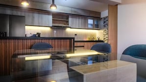 Una cocina moderna con una mesa de comedor de vidrio, armarios de madera e iluminación colgante.