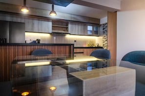 A modern kitchen with a glass dining table, wooden cabinets, and pendant lighting. - Ayra Hotel Boutique (Písac)