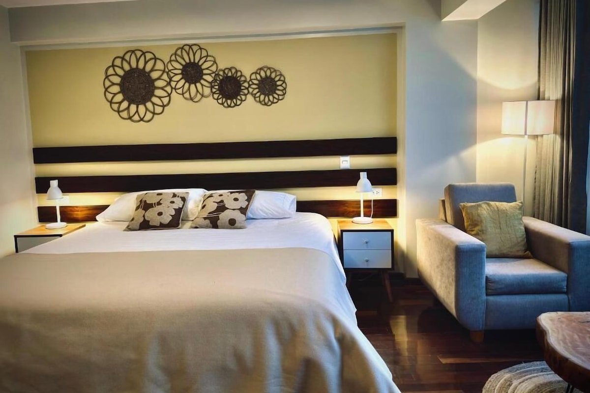 A hotel room with a large bed, two bedside tables with lamps, a sofa, and a decorative wall with floral patterns.