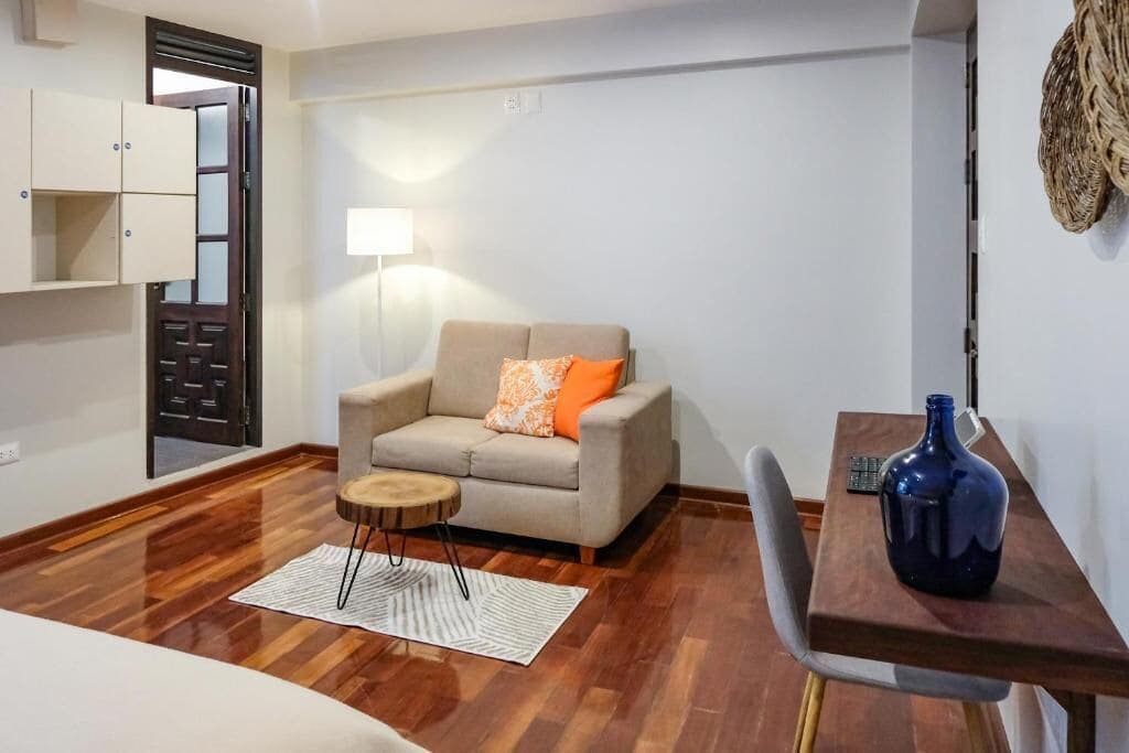 A room with a sofa, a small round table, a lamp, a chair, and a table with a vase.