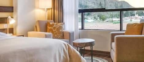 Una habitación de hotel con una cama, una mesita, una silla y vistas a la montaña.