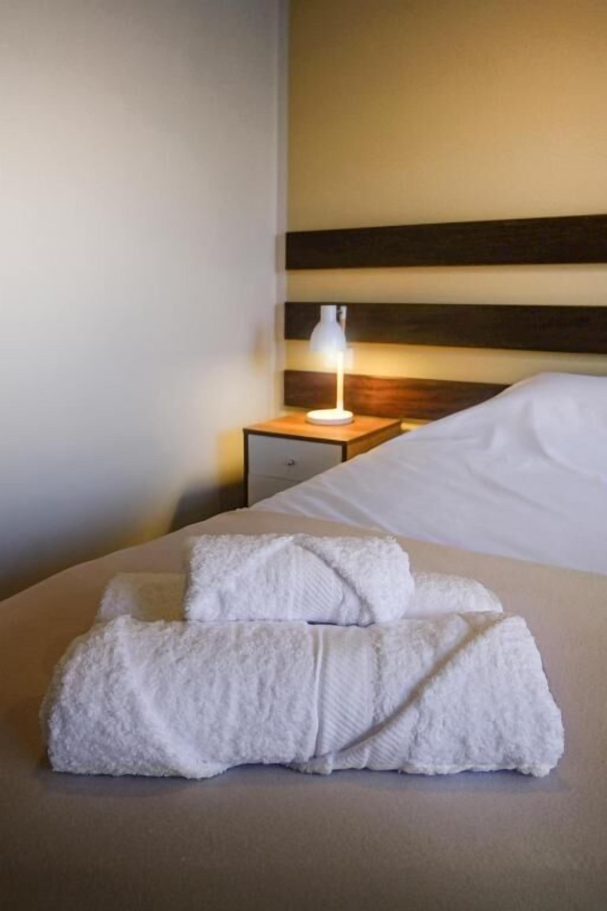 Una cama bien hecha con un edredón blanco y dos toallas dobladas sobre ella.