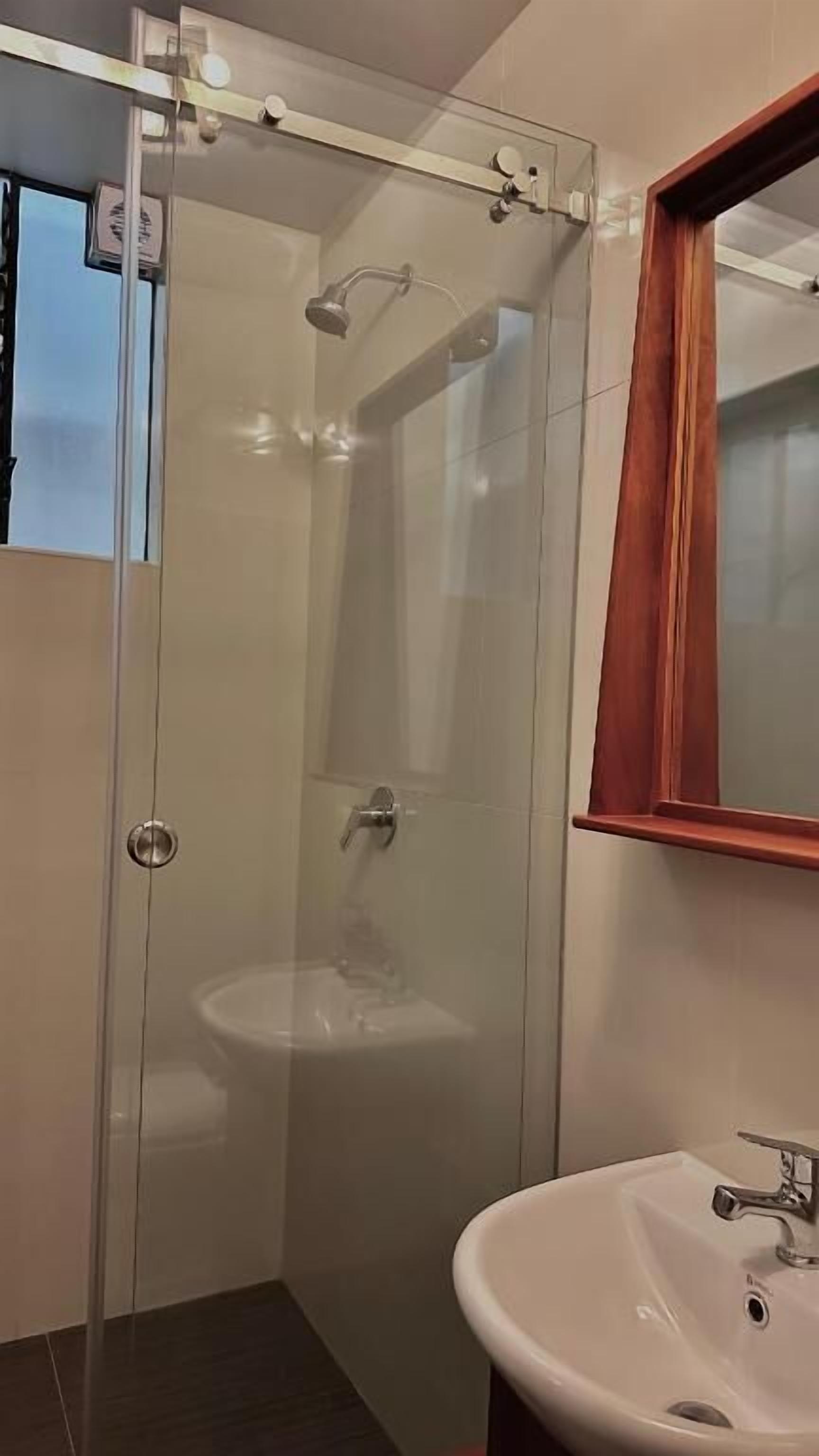 Een douche met glazen wand, een wit wastafelmeubel en een spiegel met houten lijst.