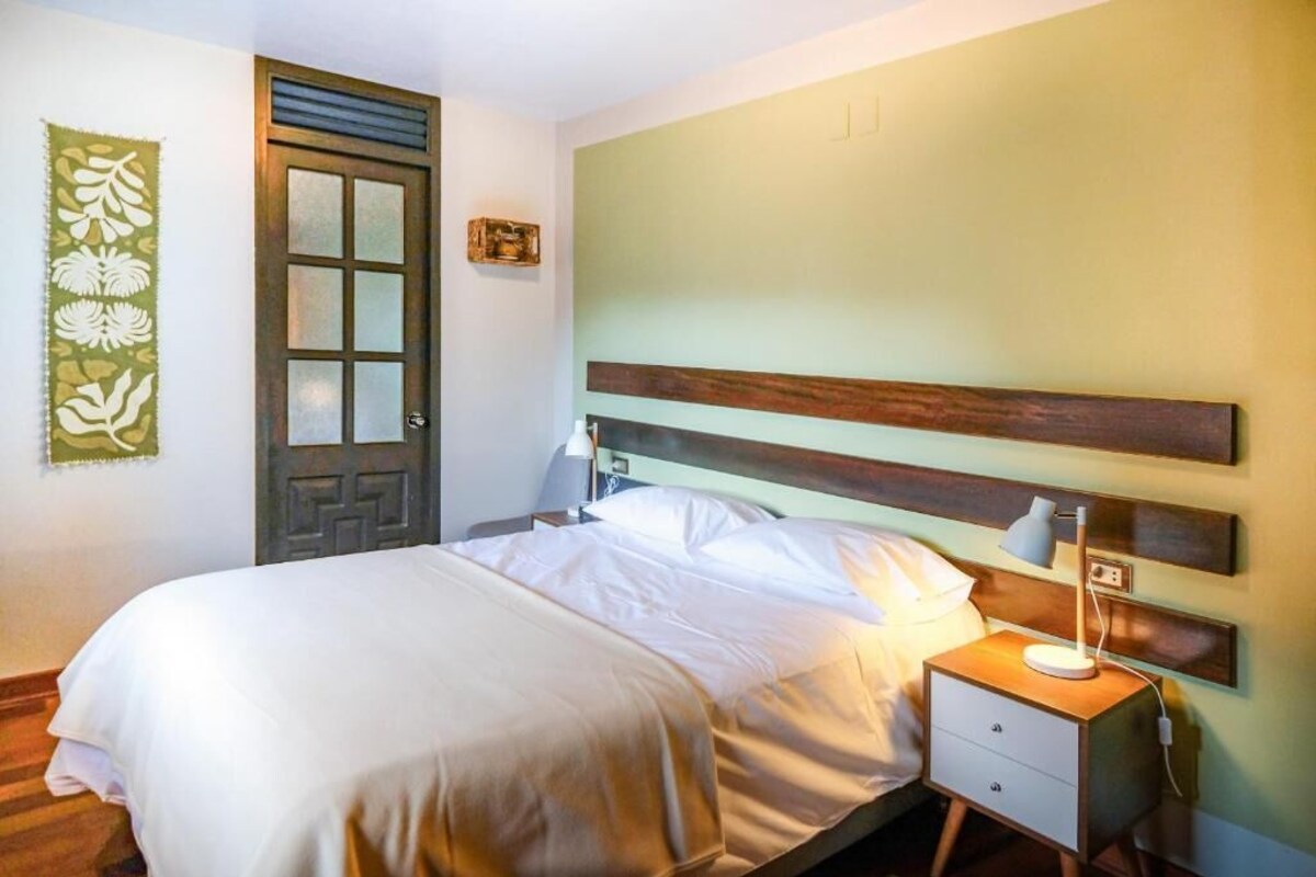 A hotel room with a bed, bedside table, lamp, and a door with a decorative panel.