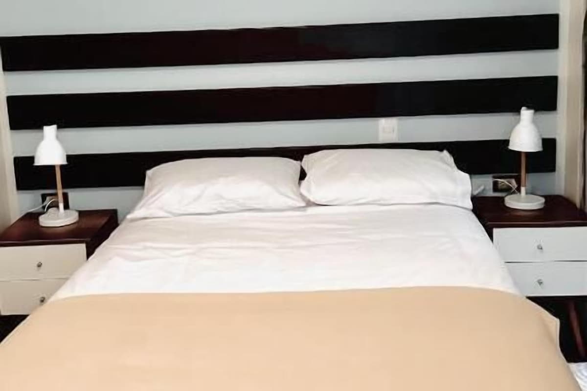 A bed with white linens, two bedside tables with lamps, and a dark headboard.