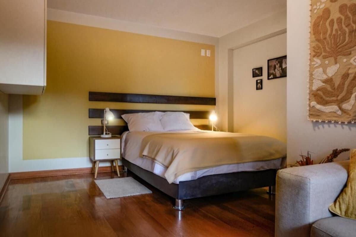 A bedroom with a bed, bedside table, lamp, and a decorative wall piece.