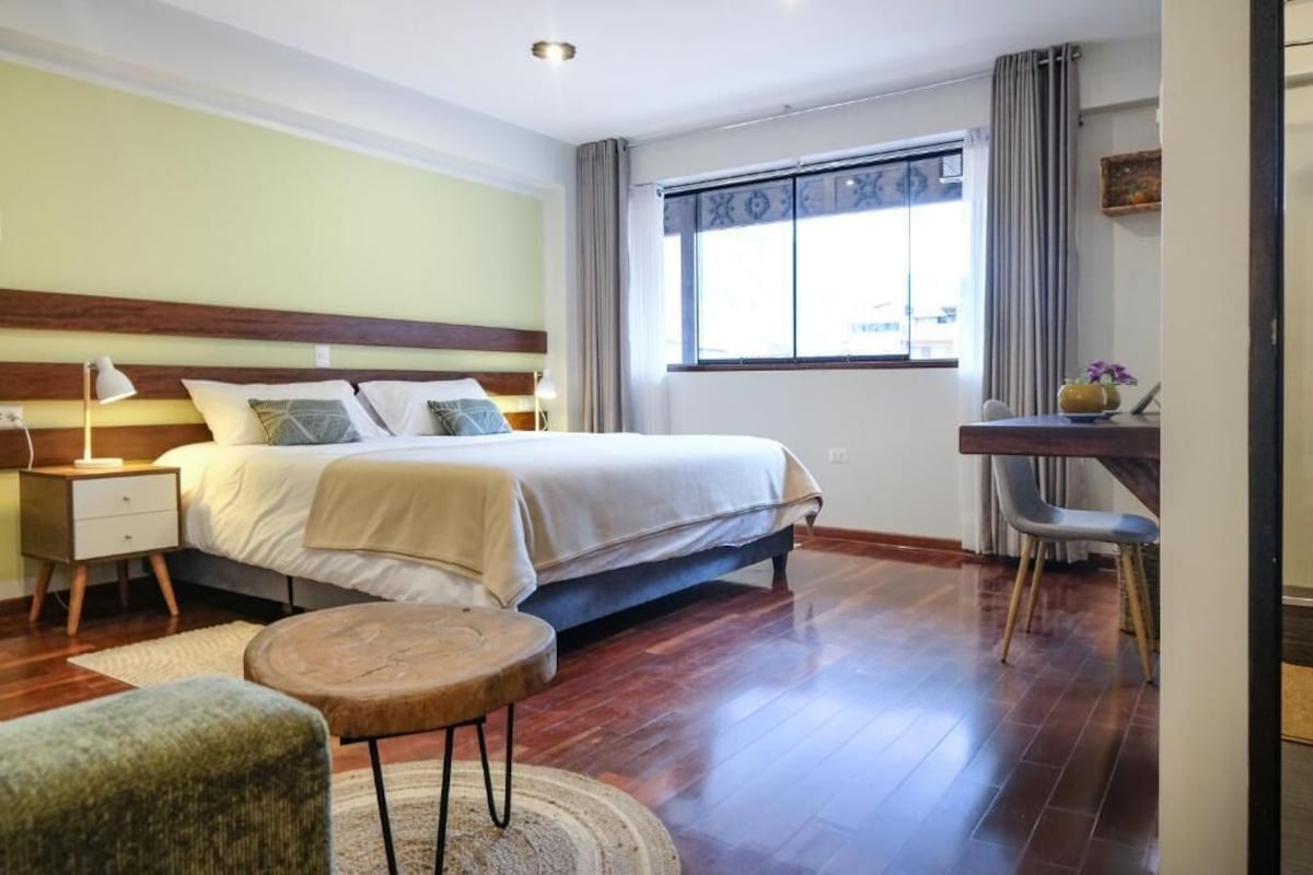 A bedroom with a bed, bedside table, lamp, chair, and a desk with a chair.