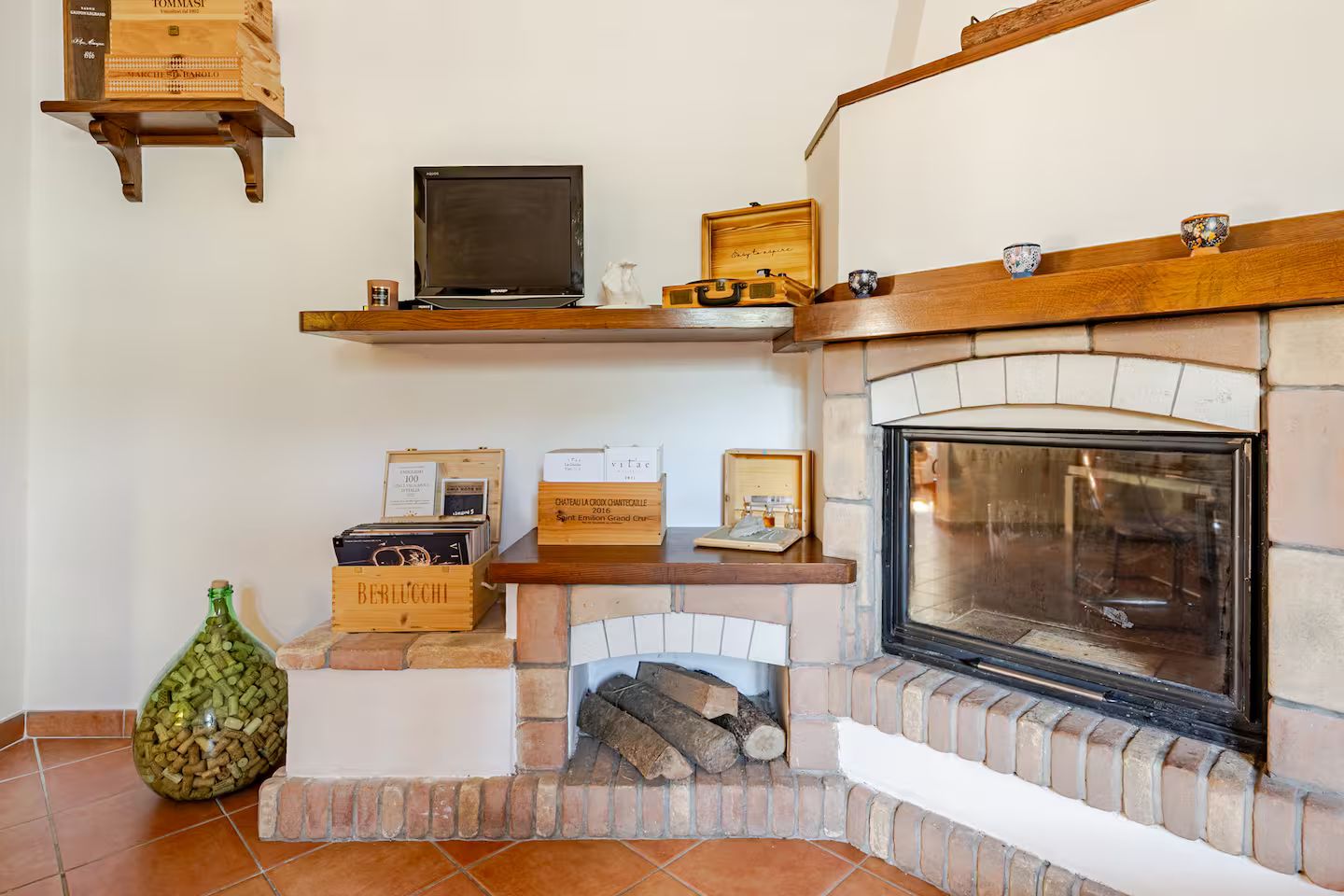 A fireplace with a stone surround, a television on a shelf above, and wine boxes on the mantel.