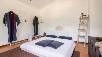A bedroom with a large bed, a wardrobe, a mirror, a shelf with decorative items, and a suitcase.