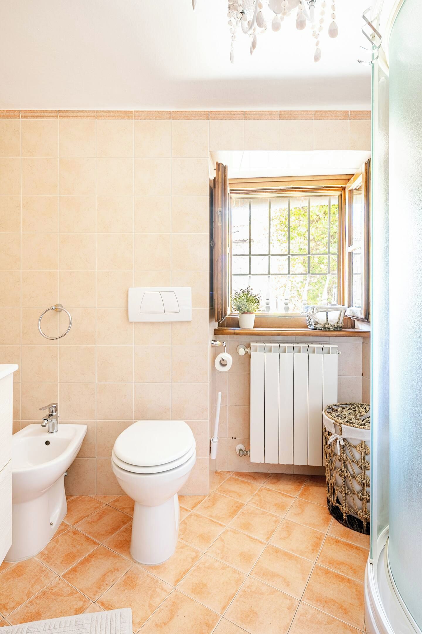 Une salle de bain équipée de toilettes, d’un bidet et d’une fenêtre donnant sur un espace verdoyant.