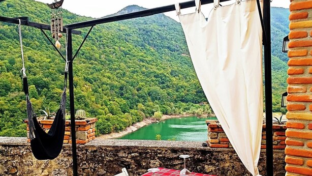 An outdoor dining area with a red checkered tablecloth, white chairs, and a view of a green valley. - Stone chalet in a medieval village, with an enchanting view of the lake (Vagli Sotto)