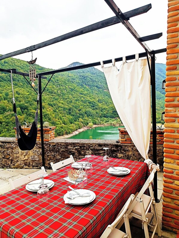 An outdoor dining area with a red checkered tablecloth, white chairs, and a view of a green valley. - Stone chalet in a medieval village, with an enchanting view of the lake (Vagli Sotto)