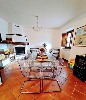 A dining area with a glass table and chairs, a fireplace, and a chandelier. - Stone chalet in a medieval village, with an enchanting view of the lake (Vagli Sotto)