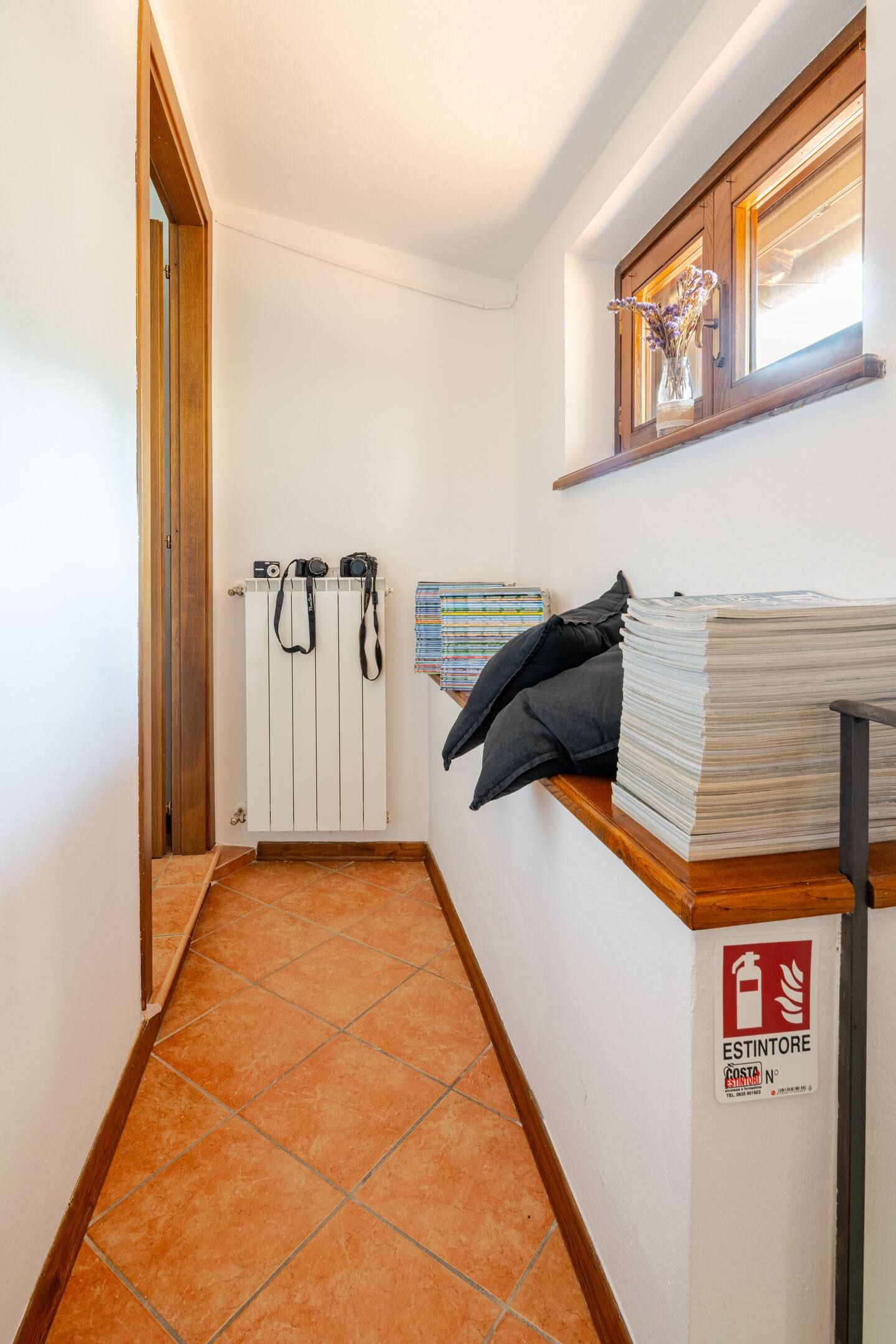 A hallway with a tiled floor, a radiator, a shelf with books, a camera, and a fire extinguisher.