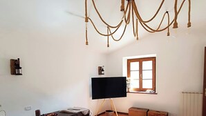 A bedroom with a bed, a television, a window, and a chandelier. - Stone chalet in a medieval village, with an enchanting view of the lake (Vagli Sotto)