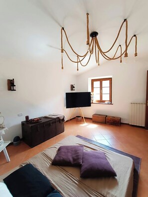 A bedroom with a bed, a television, a window, and a chandelier. - Stone chalet in a medieval village, with an enchanting view of the lake (Vagli Sotto)