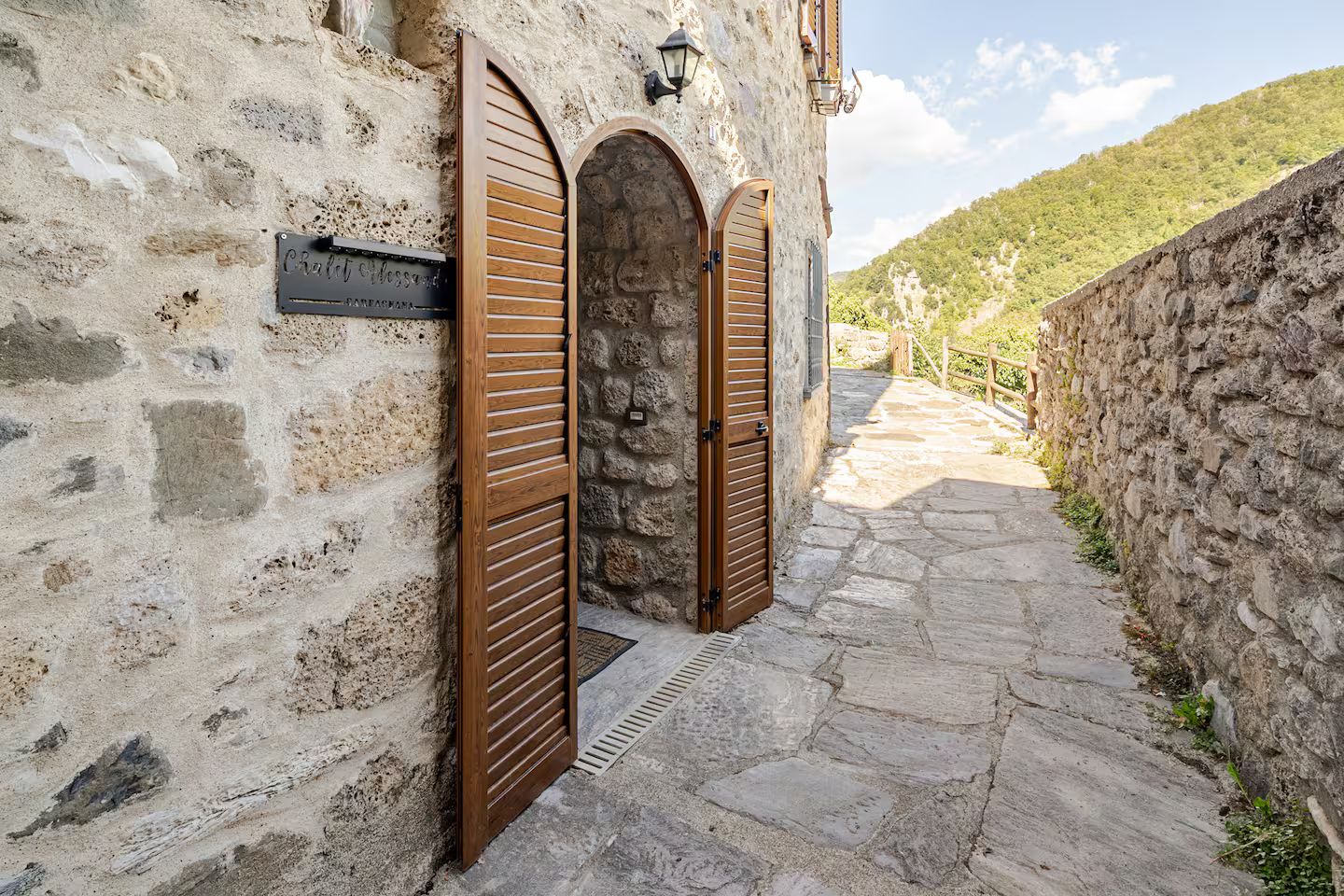 Un bâtiment en pierre doté de deux portes en bois, d’un chemin en pierre et d’un mur en pierre.