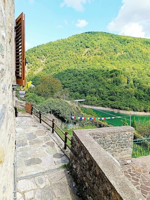 A stone staircase leading to a wooden door, with a view of a green hillside and a river.