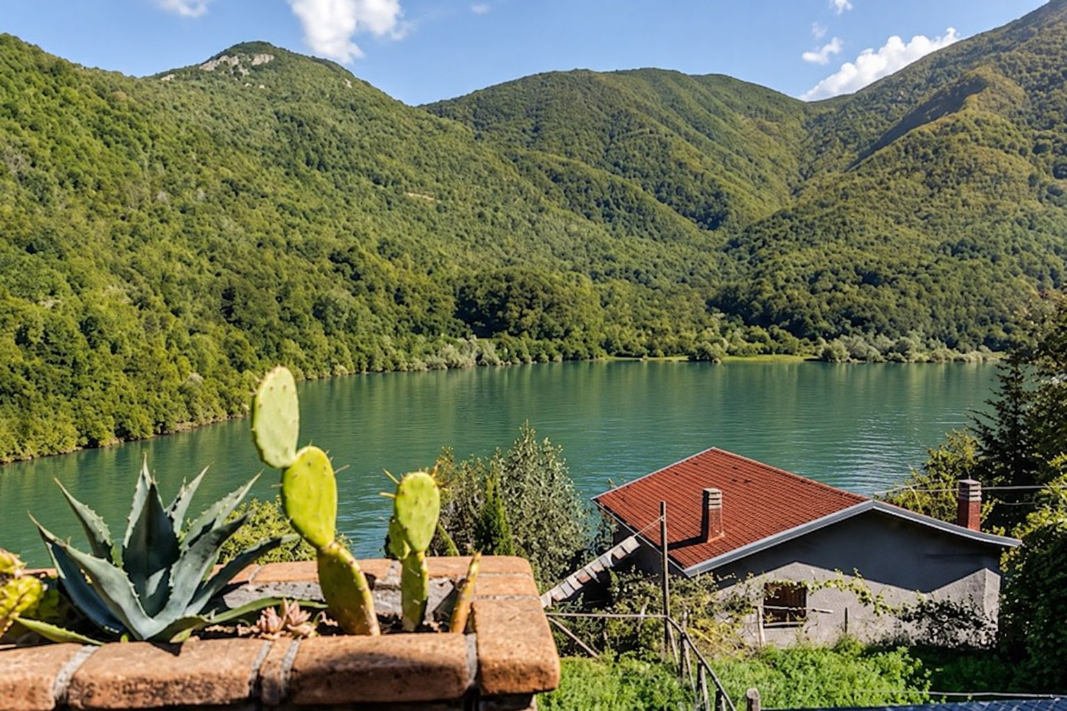 Ein Haus mit rotem Dach, einer Ziegelwand und Blick auf einen See, der von Bergen umgeben ist.