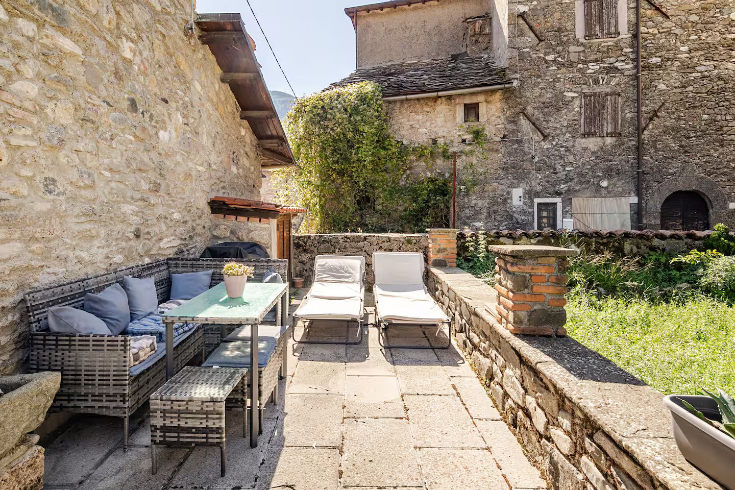 Eine Terrassengaststätte mit Korbmöbeln, einem Tisch mit einem Blumentopf und einer Steinwand.