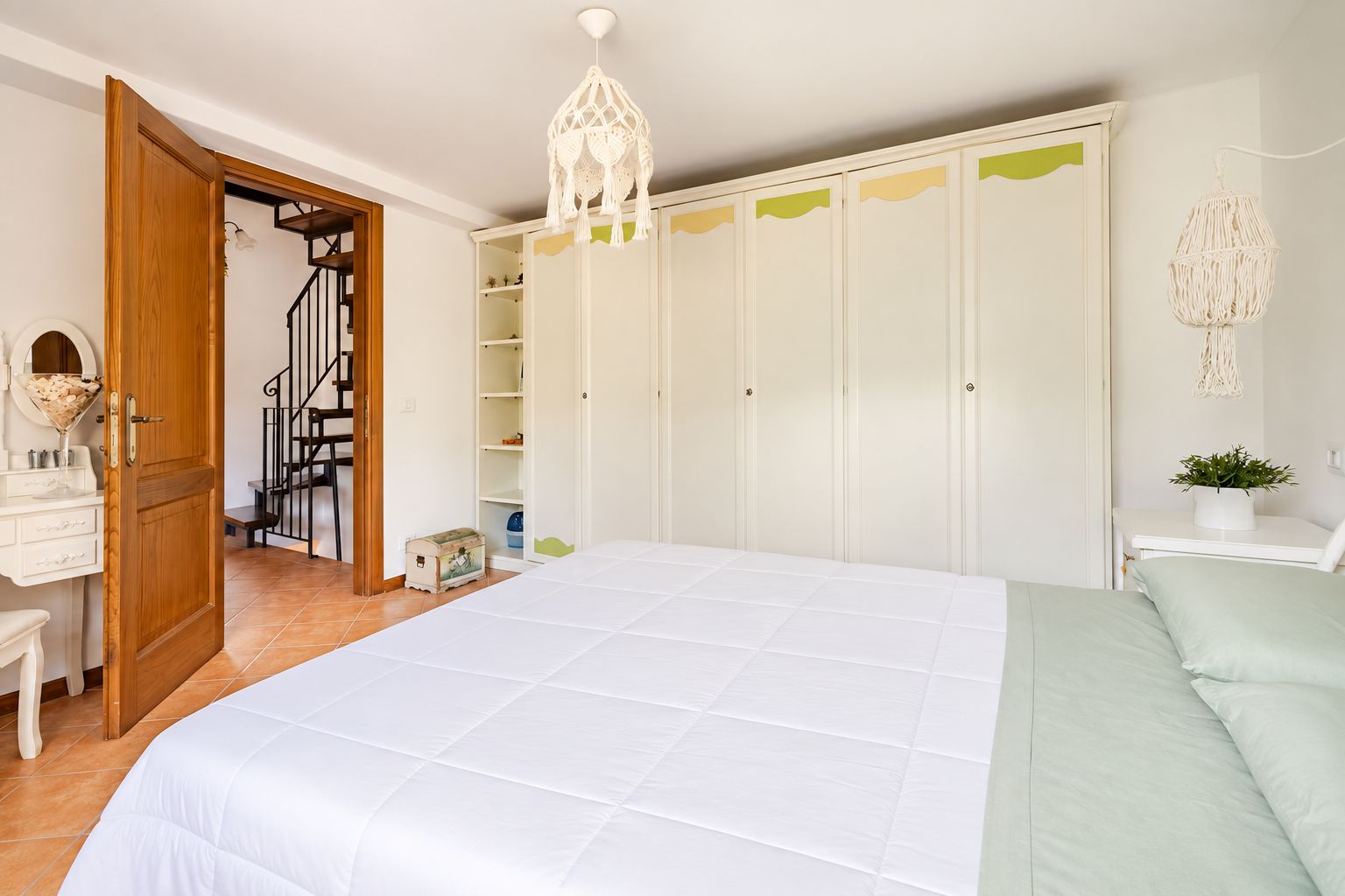 Et soveværelse med seng, garderobe, skrivebord og trappe.