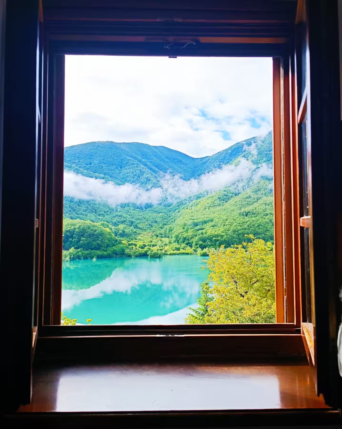 Une fenêtre donnant sur un lac, entouré de montagnes et de verdure.
