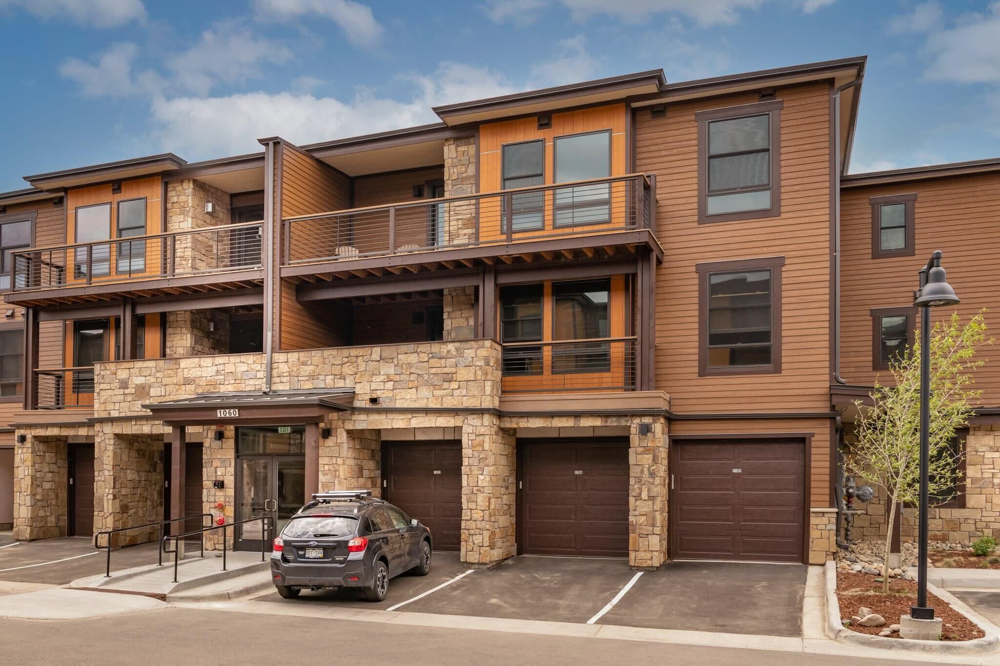 A multi-story residential building with a stone facade, a balcony on the upper floor, and a garage with two doors.