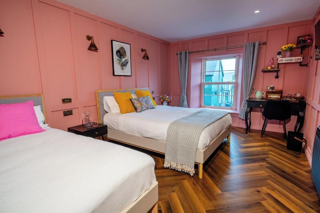 A bedroom with two beds, a window with curtains, a desk with a chair, and a shelf with decorative items.