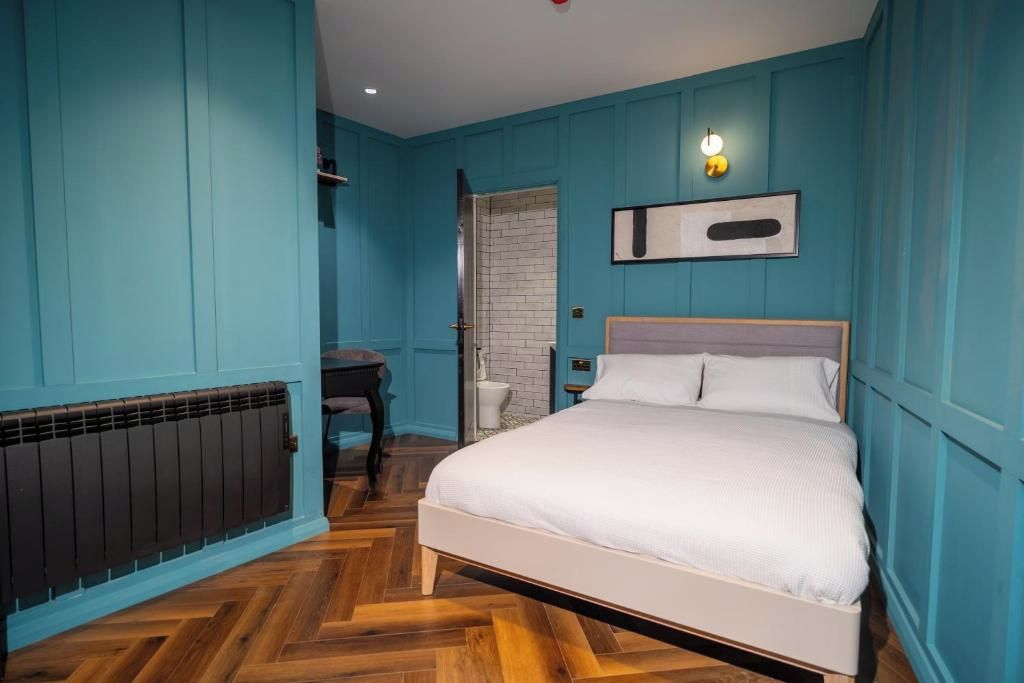 A bedroom with a bed, a radiator, a door, and a wall-mounted light fixture.
