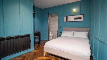 A bedroom with a bed, a radiator, a door, and a wall-mounted light fixture.