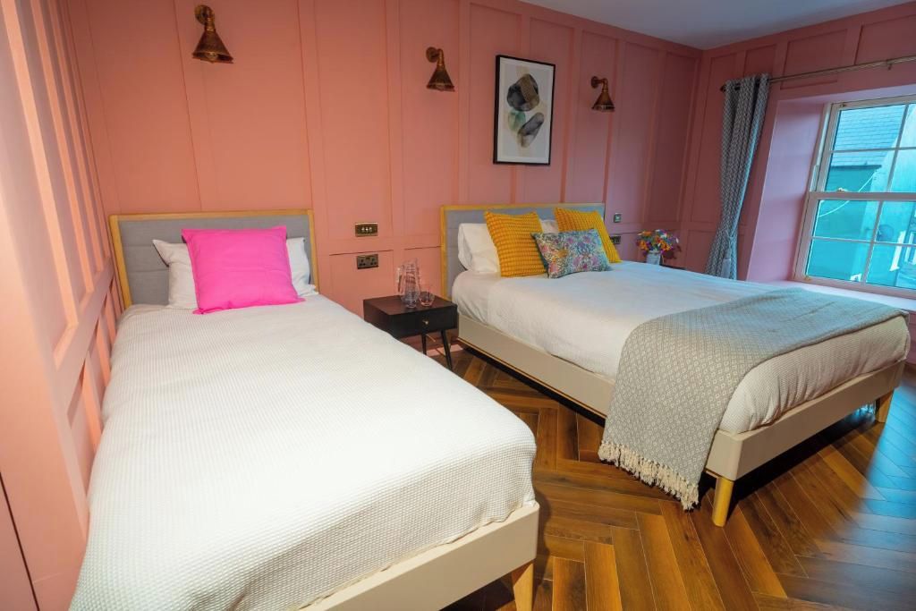 A bedroom with two beds, a nightstand, a window with curtains, and a wall-mounted light fixture.