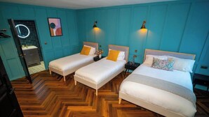 A hotel room with two single beds, a wooden herringbone floor, teal walls, and a small bathroom with a mirror and sink. - Woolen house  (MO)