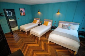 A hotel room with two single beds, a wooden herringbone floor, teal walls, and a small bathroom with a mirror and sink. - Woolen house  (MO)