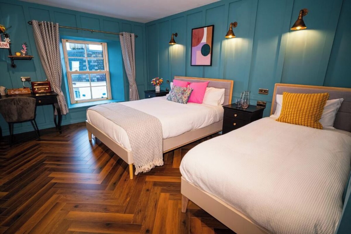 A bedroom with two beds, a desk, and a window with curtains.
